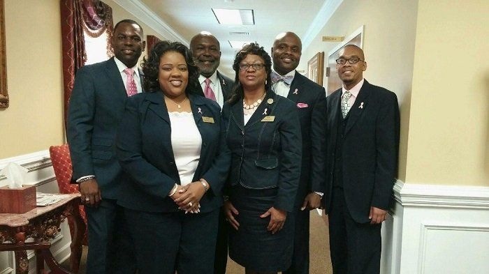 A group of six funeral directors pose together in a hallway.