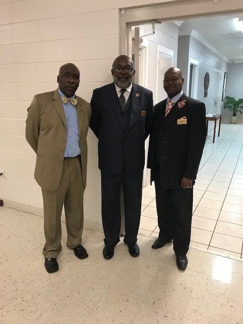Three men in suits standing side-by-side in a hallway.