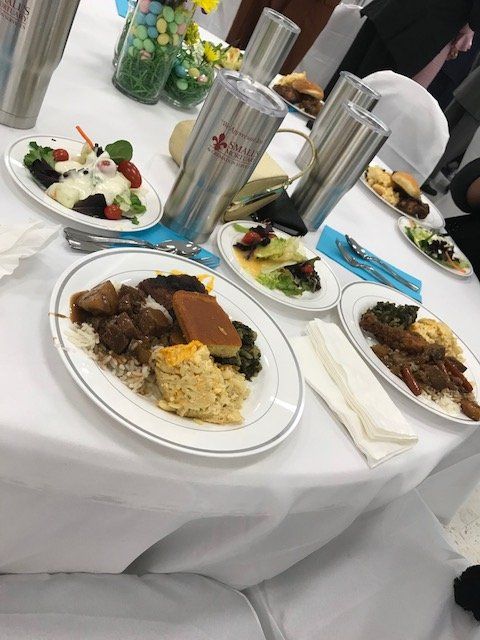 Several plates of food, salad, and tall tumblers are arranged on a white tablecloth at a formal event.