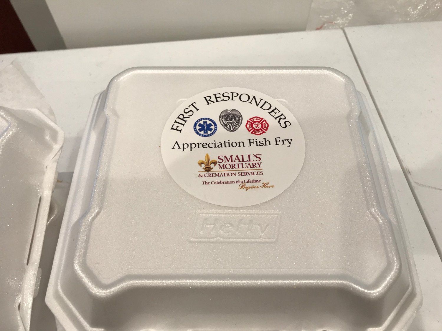 A white styrofoam takeout container with a sticker for a