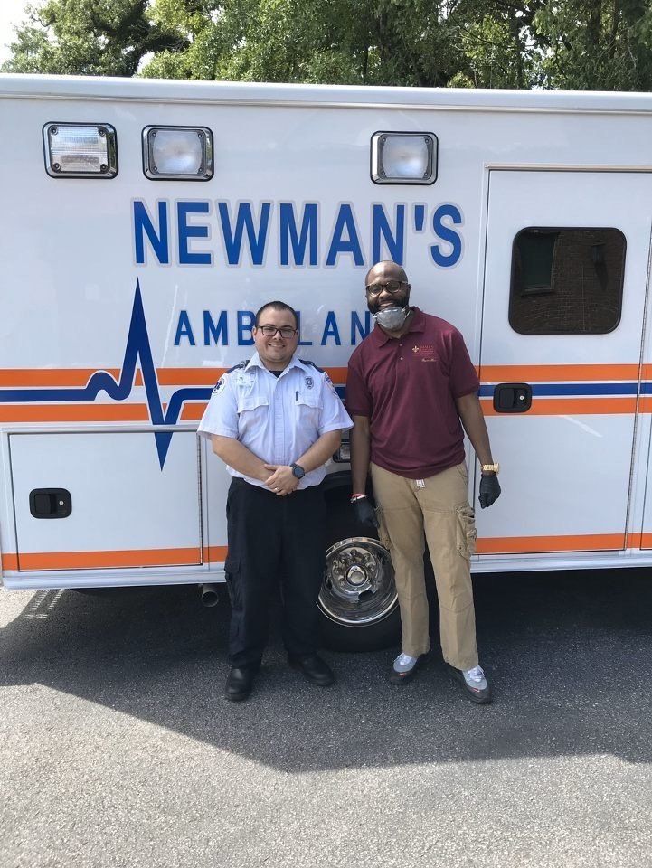 Two professionals standing in front of a white Newman’s Ambulance vehicle on a sunny day.