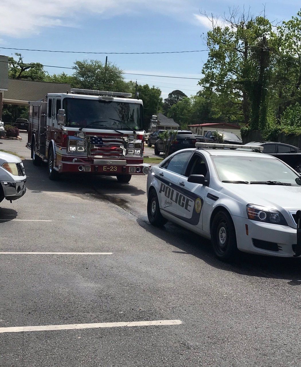 A white police cruiser and a red fire engine parked side-by-side in a paved lot under a clear, sunny sky.