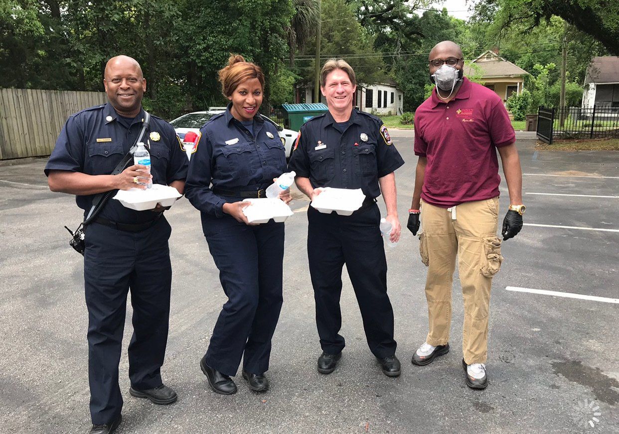 Three officers in uniform and one person in a maroon shirt stand in a parking lot, each holding a food container.