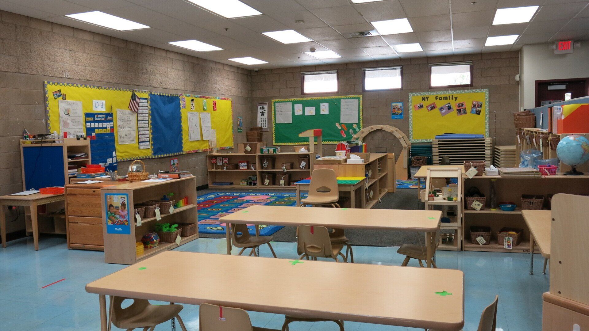 A classroom with tables and chairs and a green board on the wall.