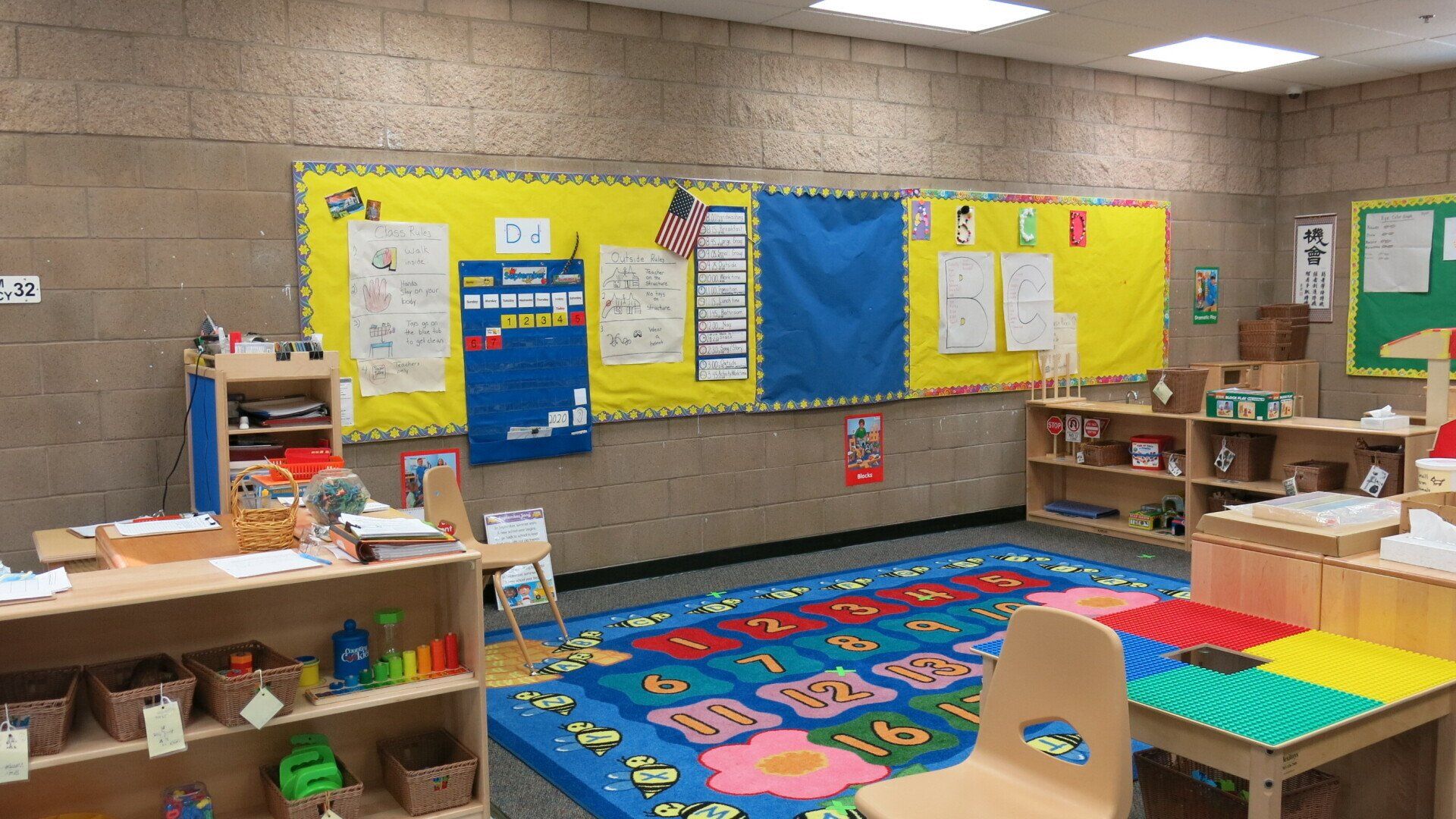 A classroom with a blue rug , tables , chairs , shelves and bulletin boards.