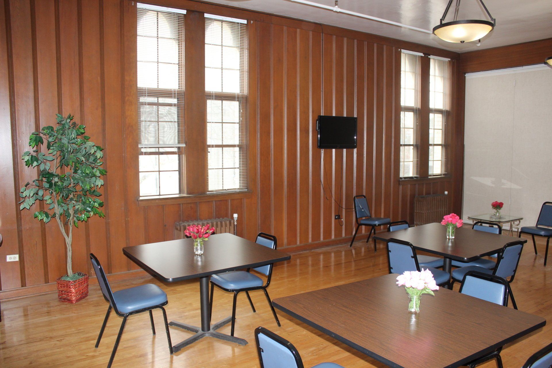 A room with tables and chairs and a tv on the wall.