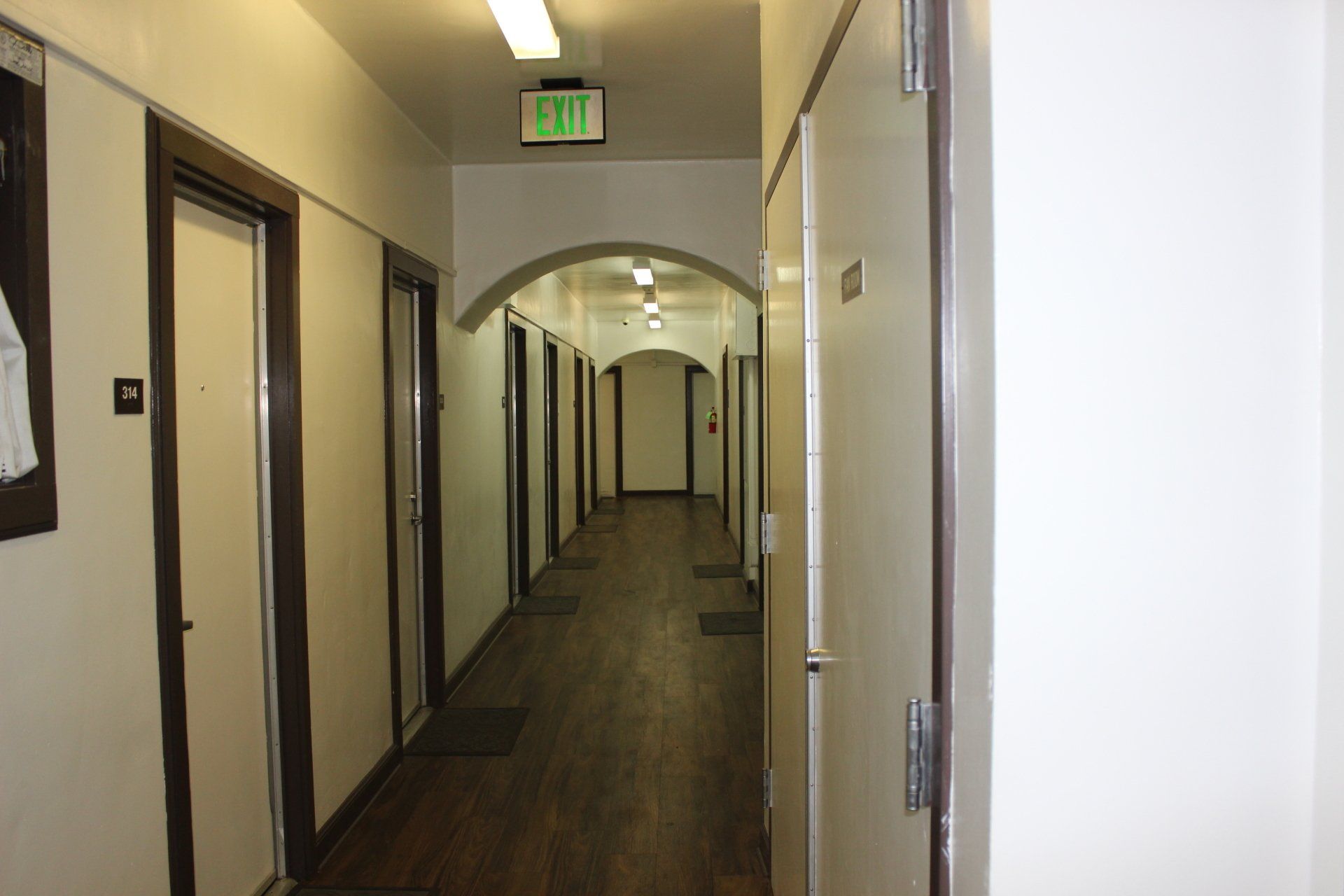A long hallway with a green exit sign on the ceiling.