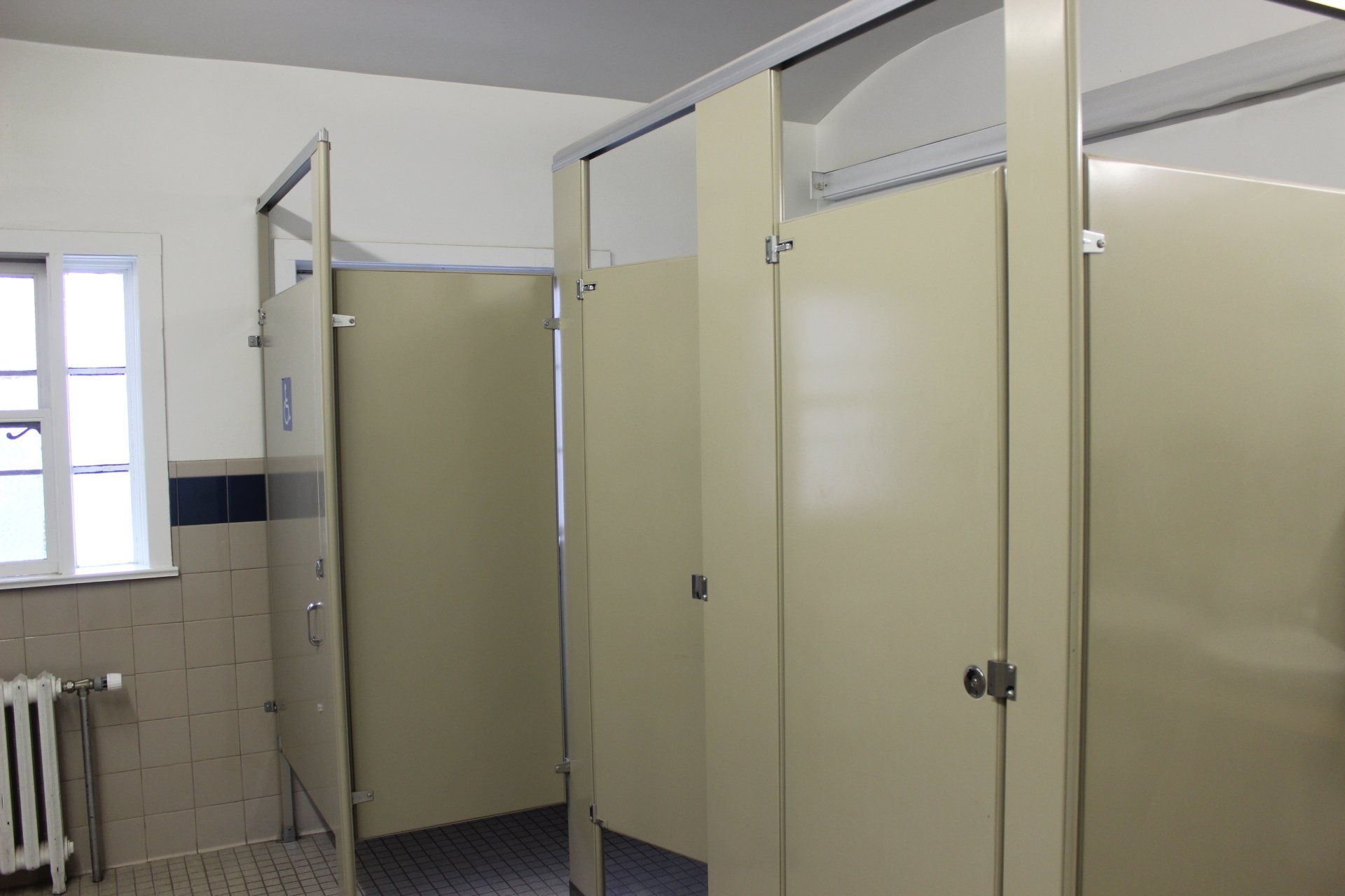 A bathroom with a lot of cubicles and a window.