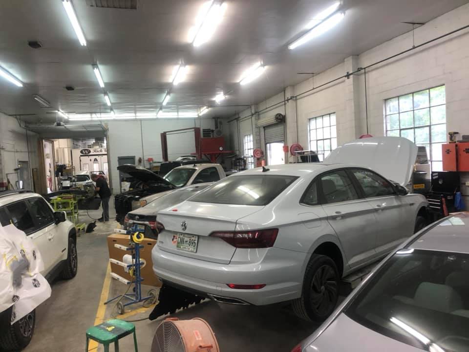 A white car is parked in a garage with its hood up.