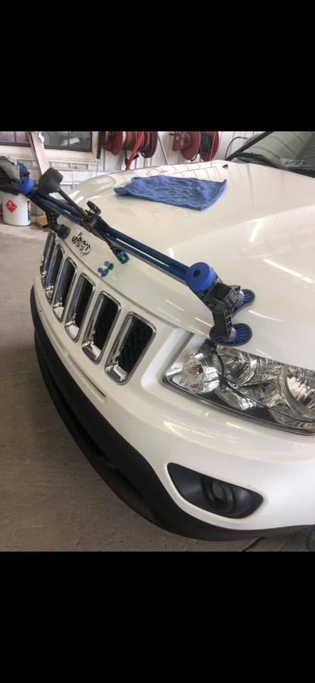 A white jeep with a blue towel on the hood is parked in a garage.