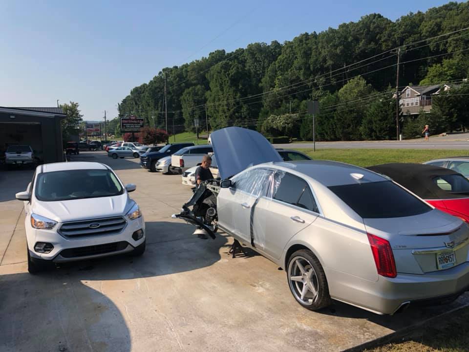 A silver car with the hood up is parked in a parking lot.