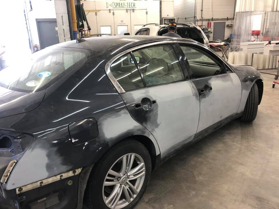 A black car is being painted in a garage.