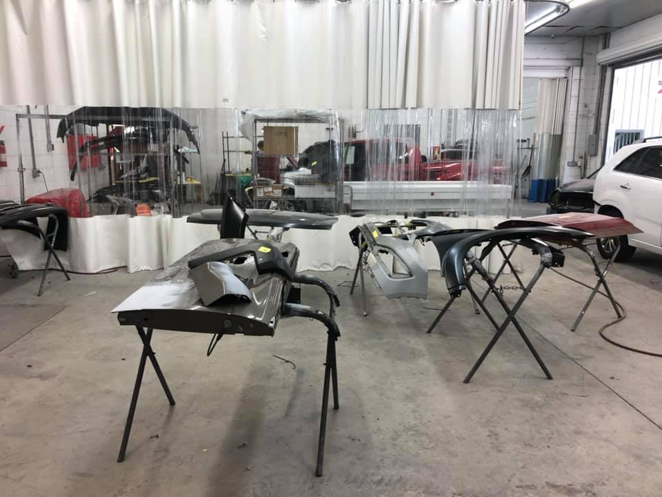 A car is being painted in a garage with tables and chairs.