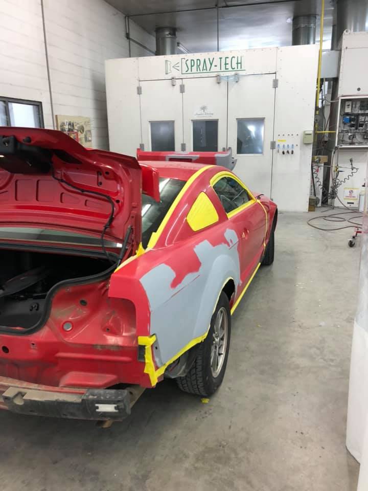 A red car is being painted in a garage.