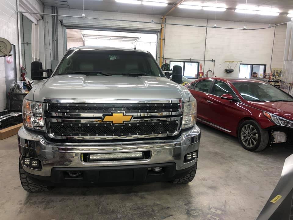 A silver chevrolet truck is parked in a garage next to a red car.