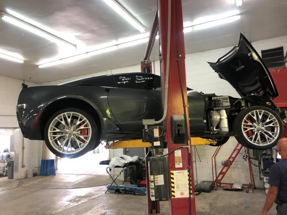 A car is on a lift in a garage with the hood open.