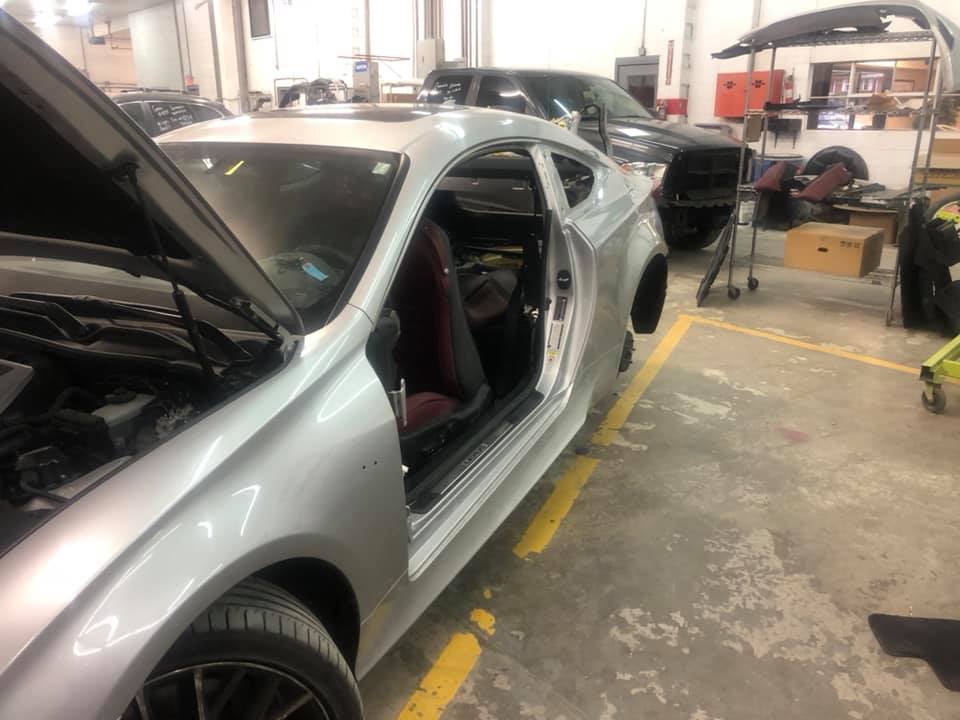A silver car with the hood open is parked in a garage.