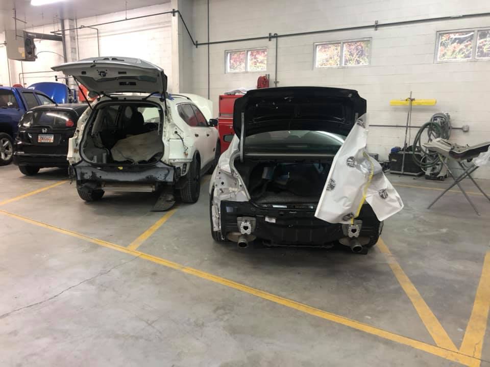 Two cars are sitting in a garage with their trunks open.