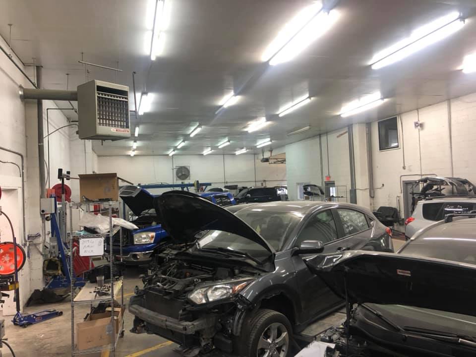 A car is being repaired in a garage with the hood open.
