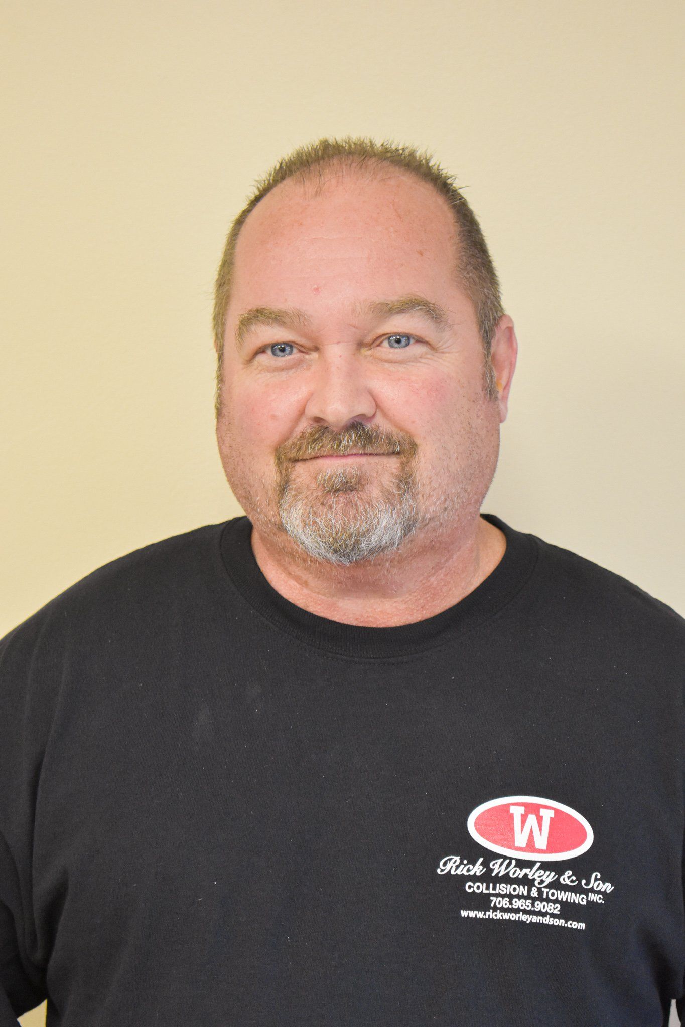 A man with a beard is wearing a black shirt with the letter w on it.