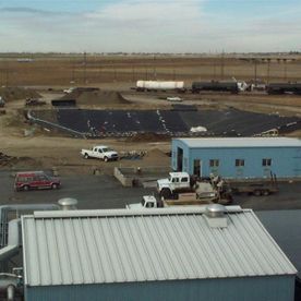 Industrial site with trucks, building, and black-lined pit against a brown field.