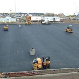 Construction site, workers and equipment paving asphalt. Yellow rollers compacting new black pavement.