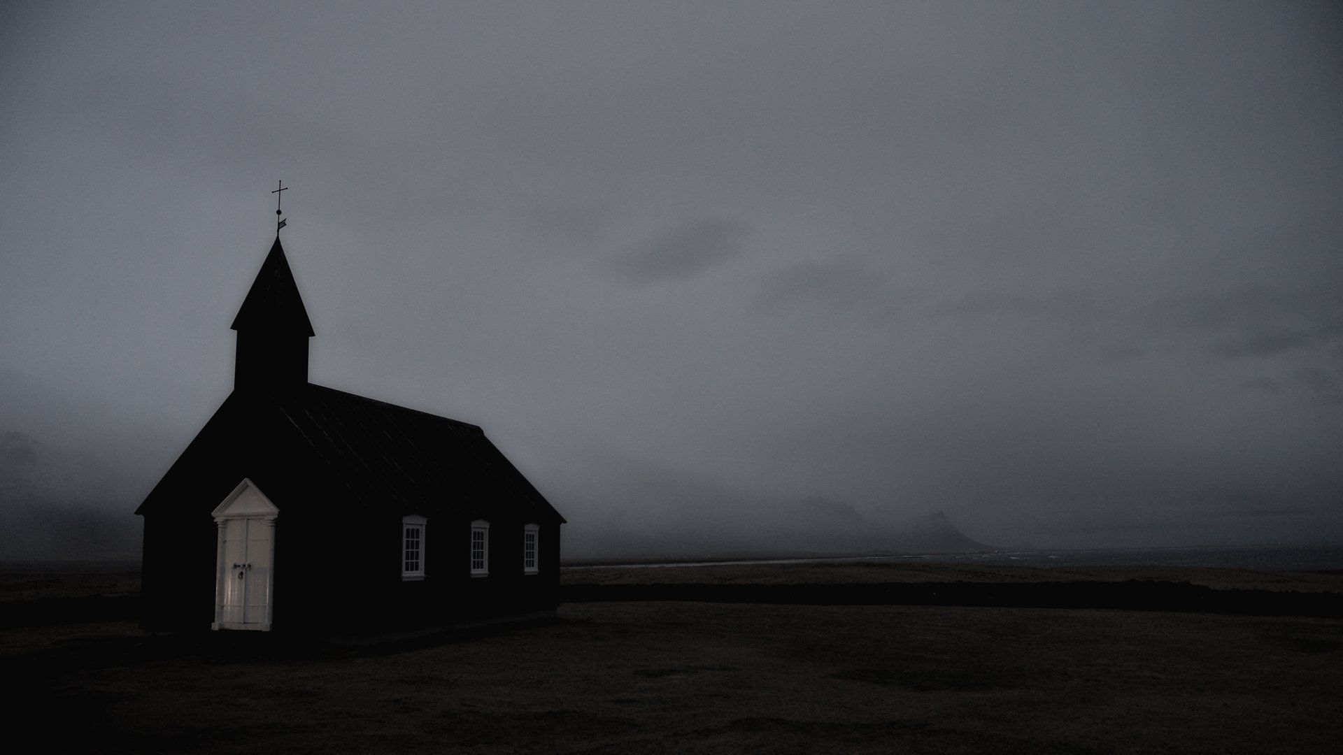 A black and white photo of a small church in the middle of a field.