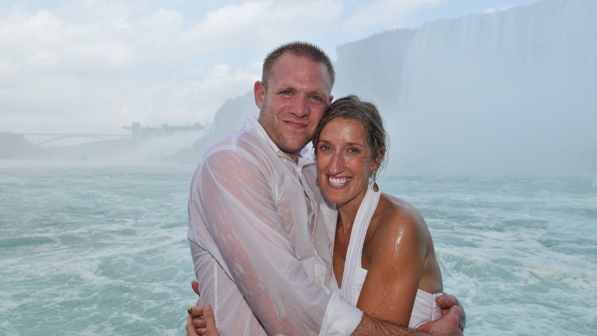 A man and a woman are posing for a picture in front of a waterfall.