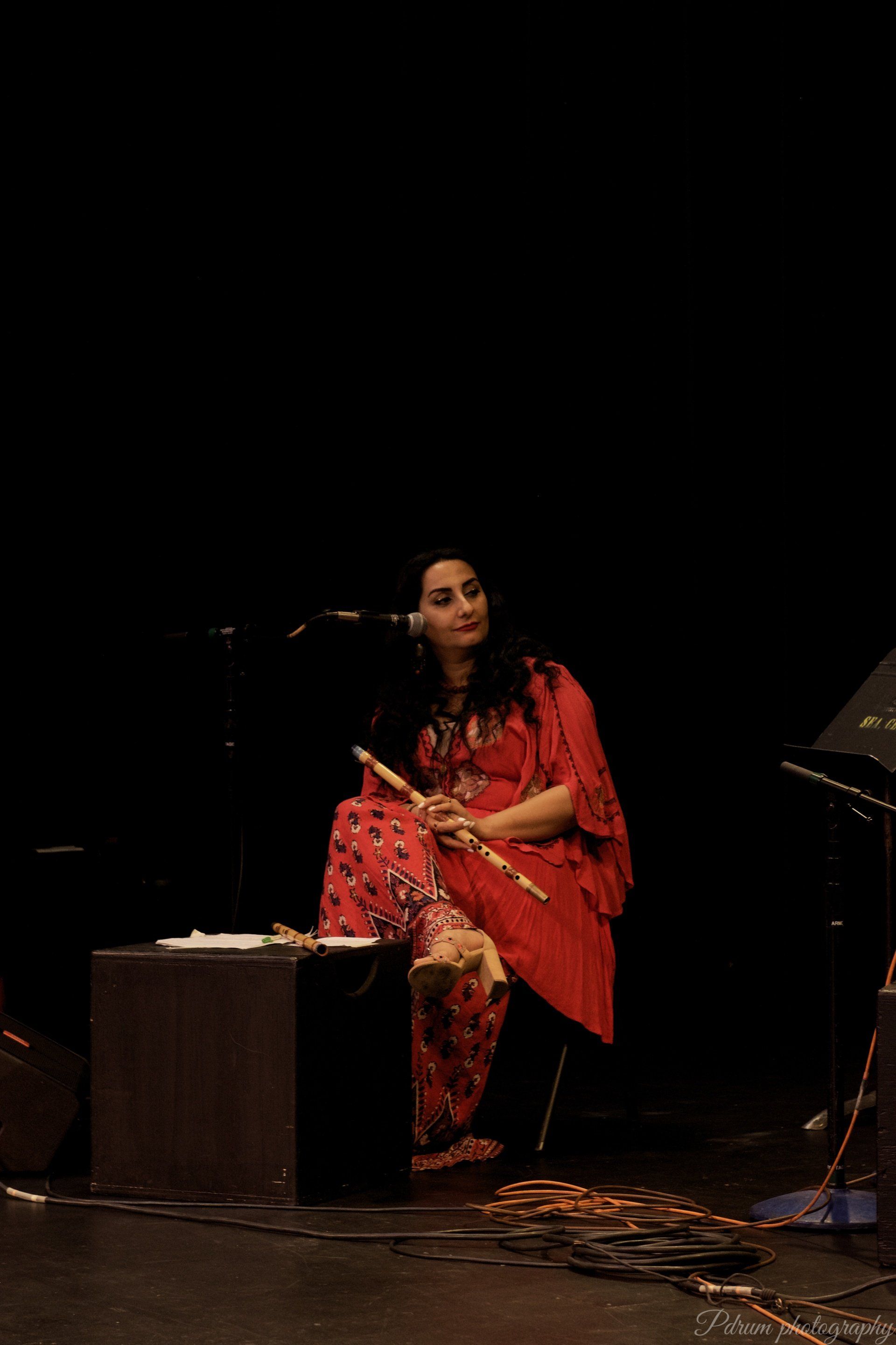 A woman in a red dress is sitting on a stage playing a flute.
