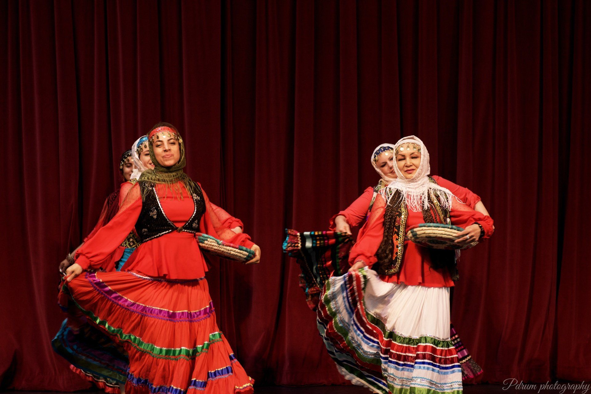 A group of women are dancing on a stage in front of a red curtain.