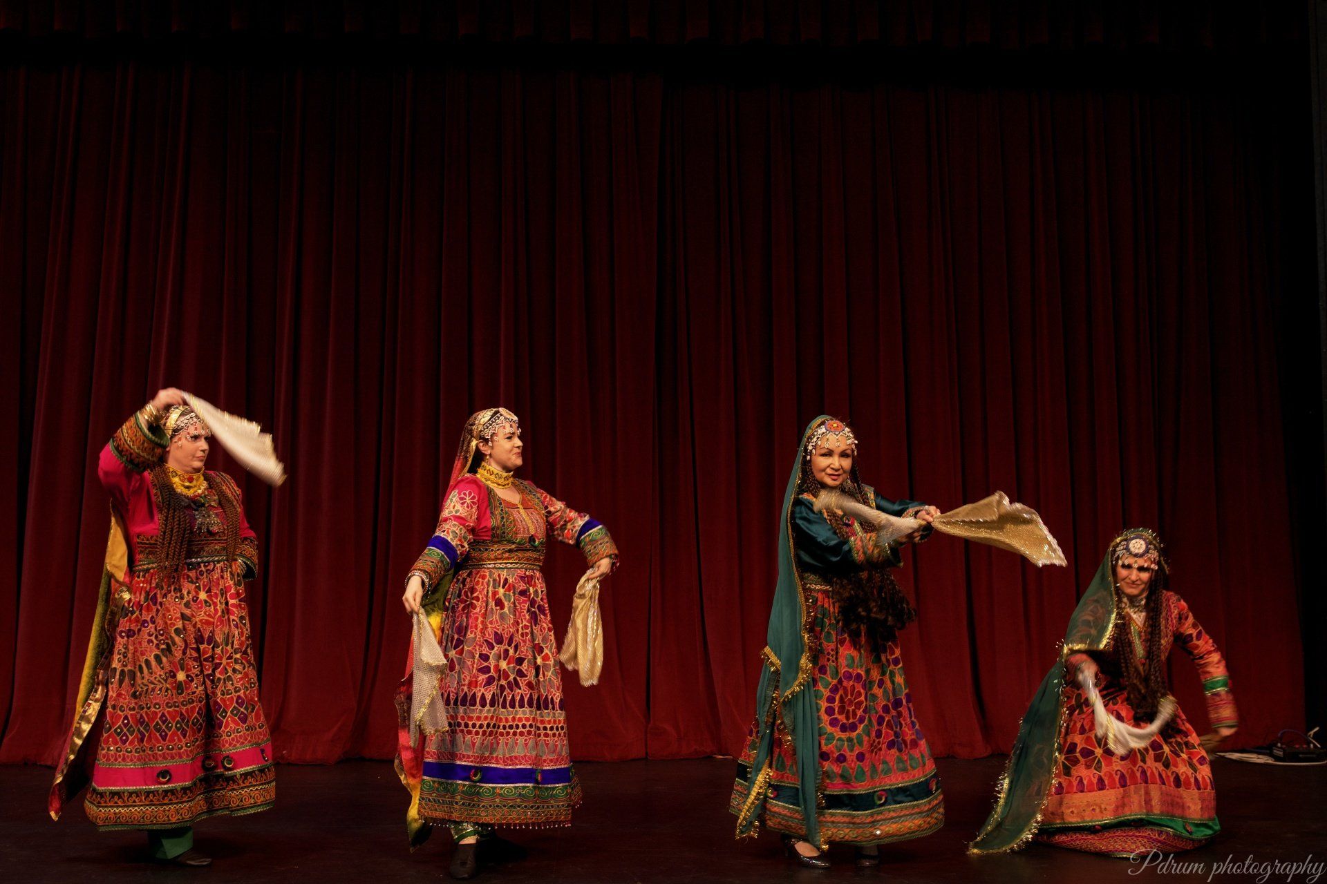 A group of women are dancing on a stage in front of a red curtain.