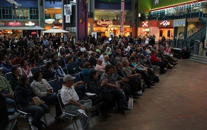 A large group of people are sitting in chairs in a mall.