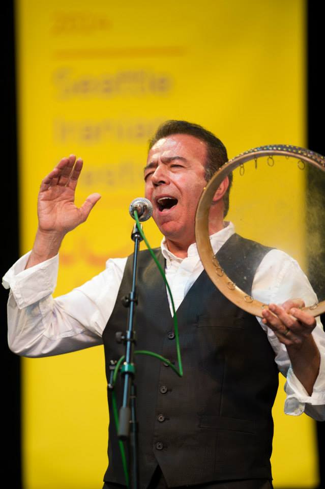A man is singing into a microphone while holding a tambourine.
