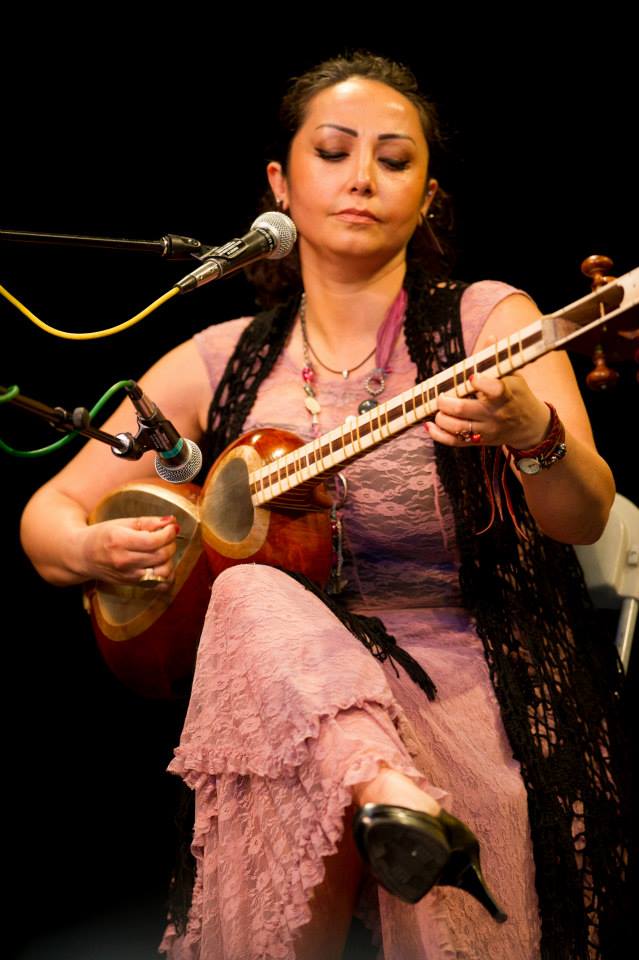 A woman in a pink dress is playing a guitar in front of a microphone.
