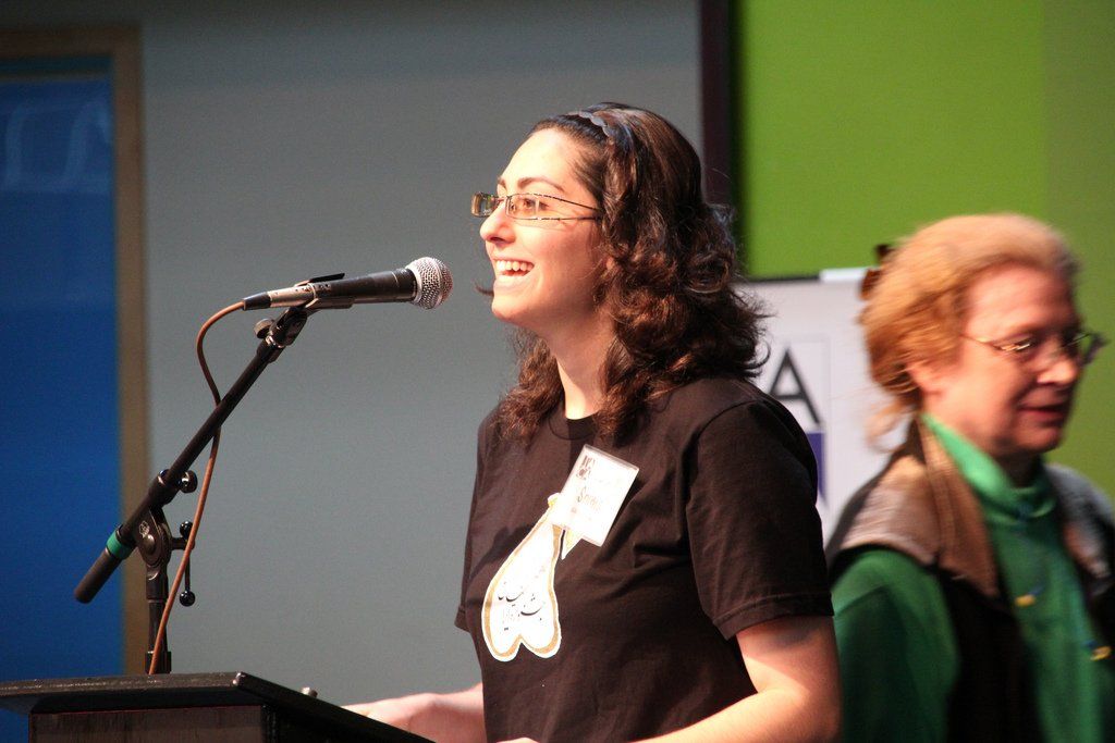 A woman stands at a podium speaking into a microphone