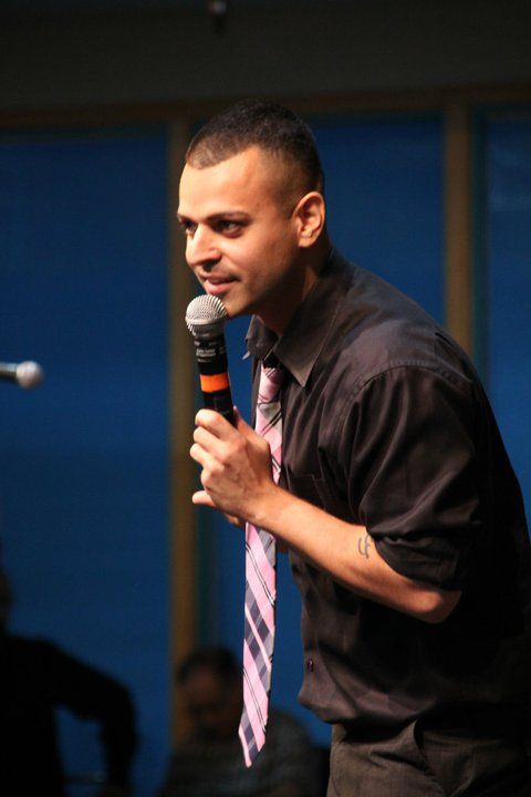 A man in a black shirt and tie is holding a microphone