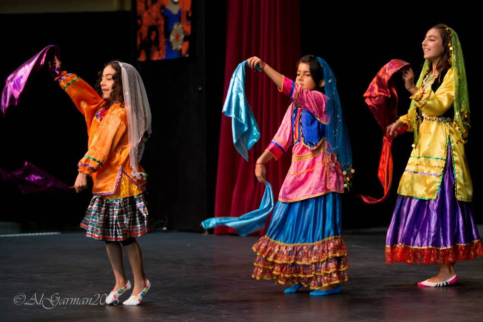 Three girls in colorful dresses are dancing on a stage.