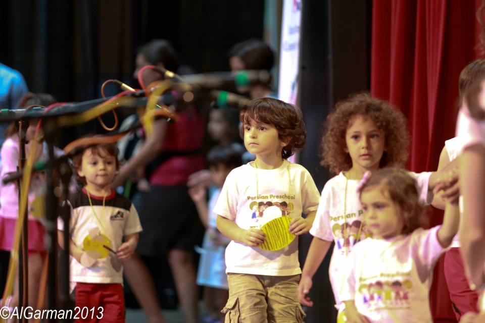 A group of children are standing in front of a red curtain.