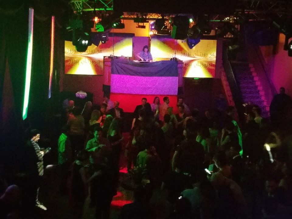 A crowd of people are gathered in a dark room at a party
