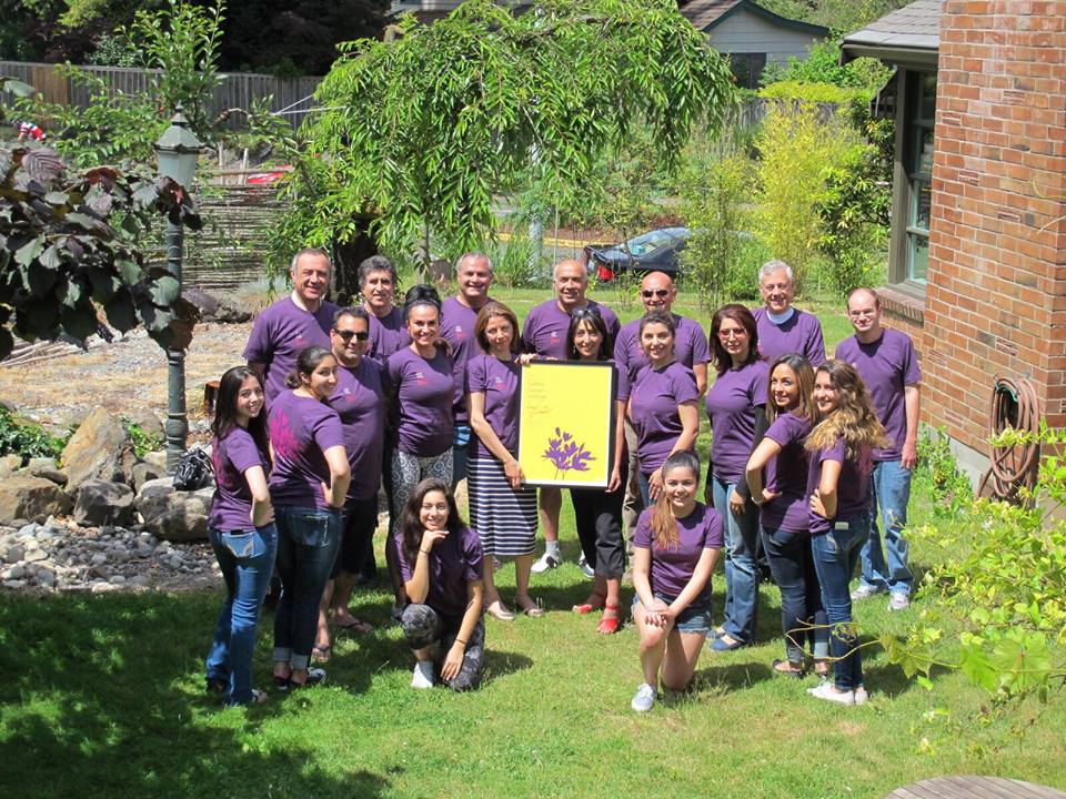 A group of people in purple shirts are posing for a picture in a yard.