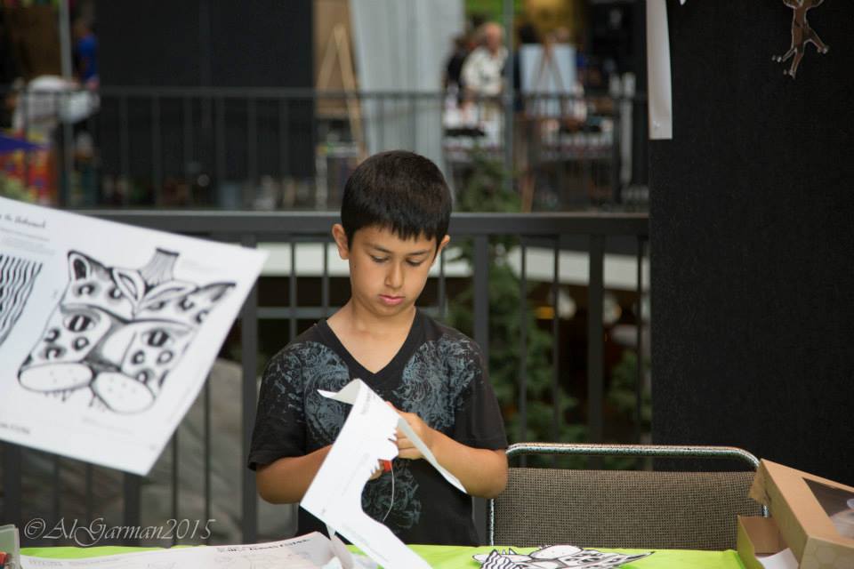 A young boy is sitting at a table cutting a piece of paper.