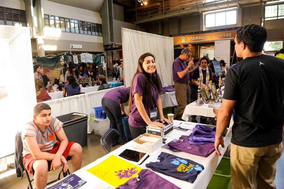 A group of people are standing around a table with purple shirts on it.