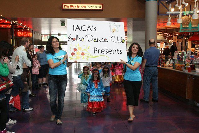 Two women holding a sign that says iaca 's alpha dance club presents