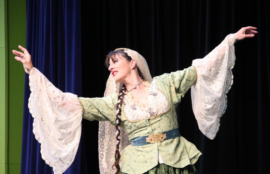 A woman in a green and white dress is dancing on a stage.