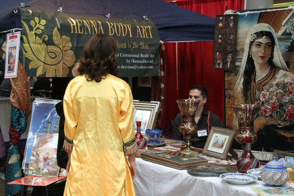 A woman in a yellow dress stands in front of a sign that says henna