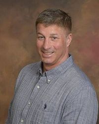 Ron Bardwell - President Man smiling, wearing a blue button-down shirt, neutral background.