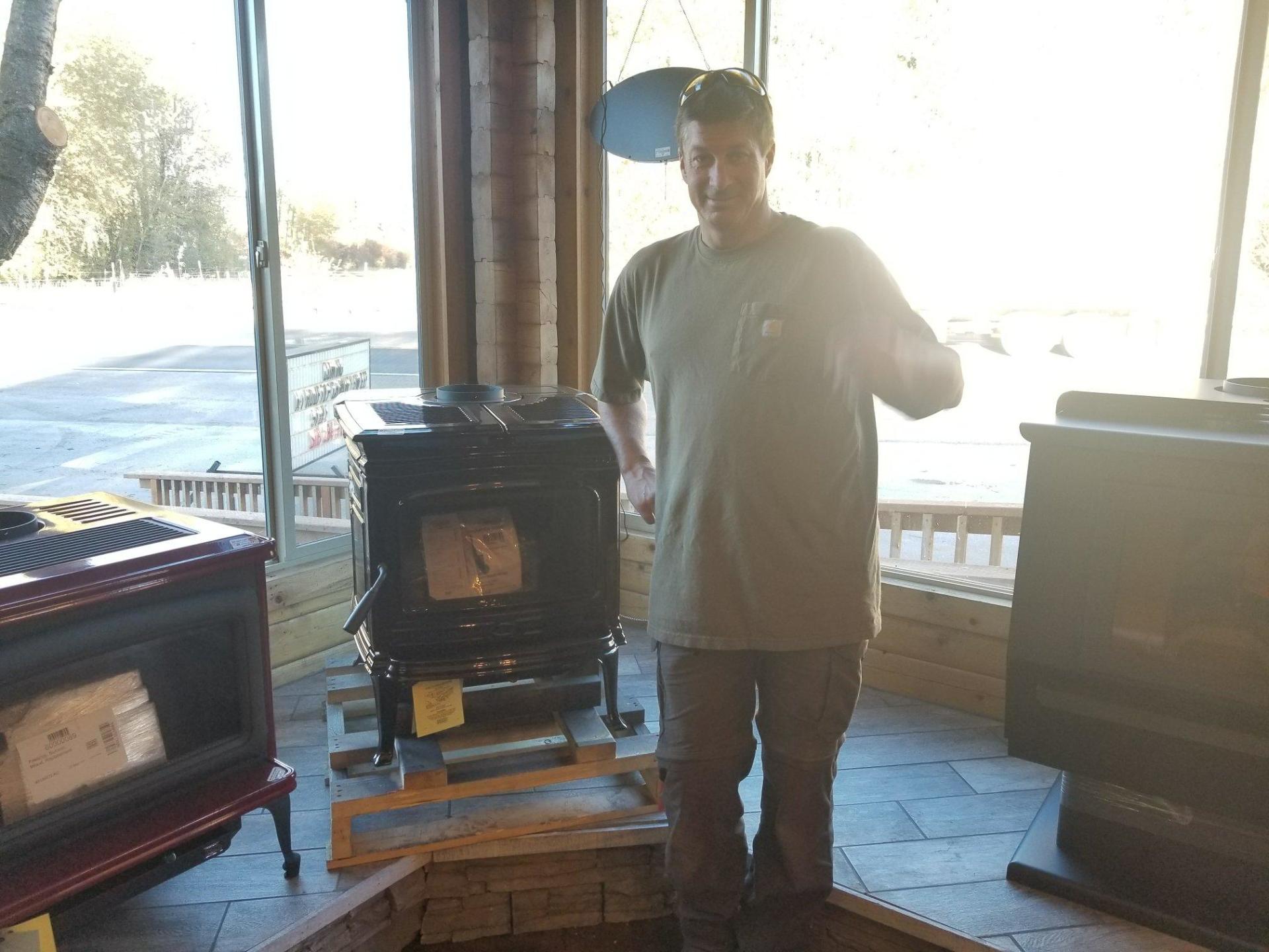 Man stands next to a black stove in a showroom. He points. Other stoves are also displayed.