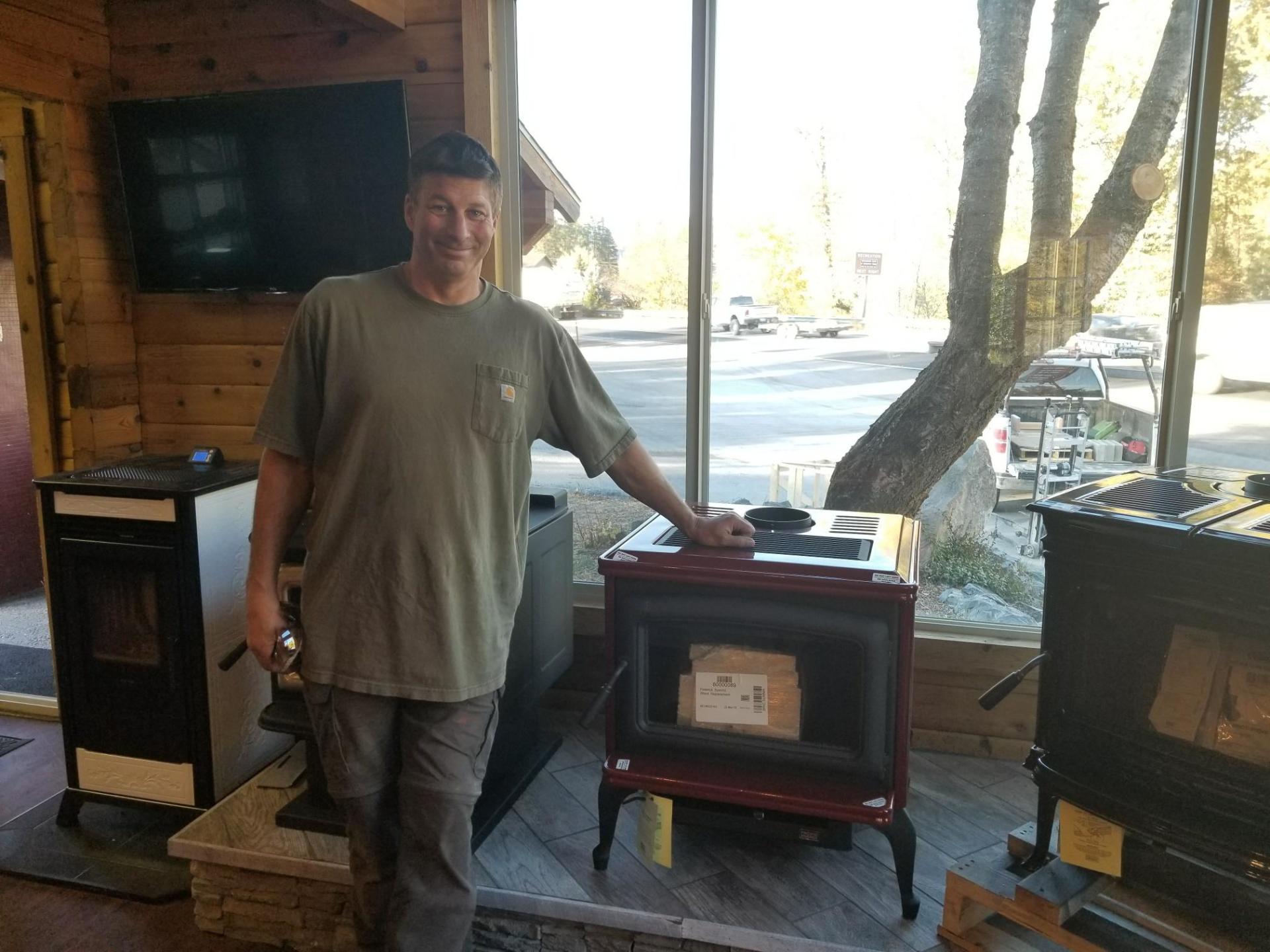 Man standing by red and black stove in a showroom.