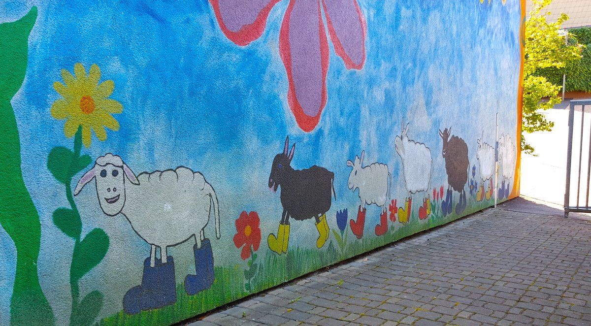 Wandgemälde mit Schafen und Blumen auf strukturierter blauer Wand, farbenfrohes Design.