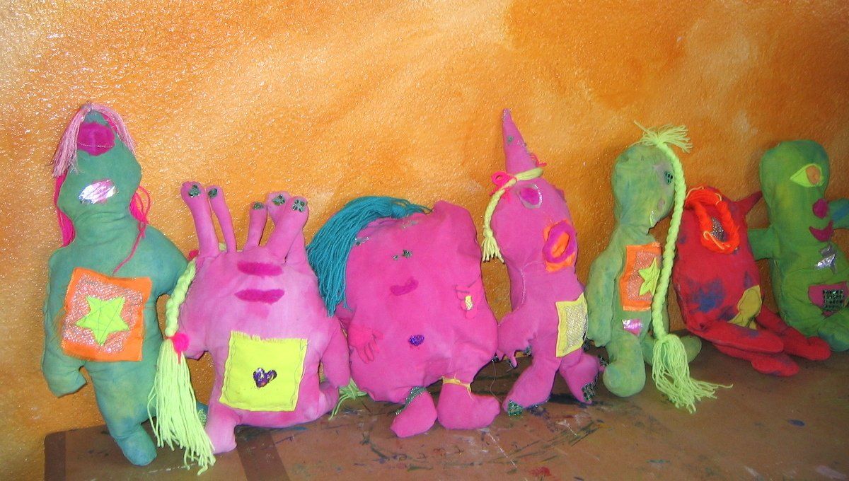 Bunte, handgefertigte Monster-Plüschtiere stehen an einer orangefarbenen Wand.
